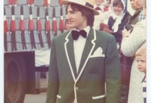 Man in green jacket and bow tie walking next to a float